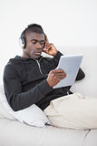 Casual man sitting on his sofa listening to music on tablet pc
