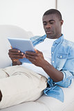 Casual man lying on sofa using his tablet pc