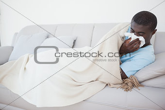 Sick man lying on sofa under a blanket