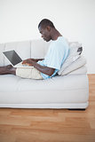 Casual man lying on sofa using laptop