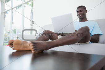 Casual man sitting on sofa using laptop with feet up