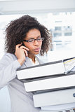 Casual businesswoman talking on phone holding pile of documents
