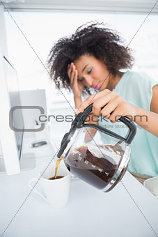 Tired businesswoman pouring a cup of coffee at desk