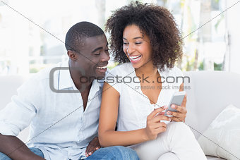 Attractive couple sitting on couch together looking at smartphone