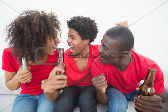Football fans in red sitting on couch with beer cheering