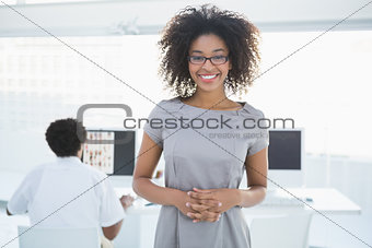 Young pretty editor smiling at camera with colleague working behind her