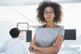 Young pretty editor looking at camera with colleague working behind her