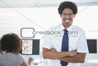 Young handsome editor smiling at camera with colleague working behind him