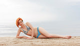 Portrait of a beautiful young red-haired woman in bikini lying on the beach