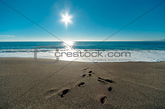 Sunny day, blue sea and footprints in the sand