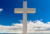 White cross against blue sky and fluffy clouds