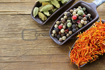 spices (saffron, pepper and cardamom) in the scoop on a wooden table