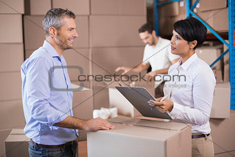 Warehouse manager writing on clipboard talking to colleague