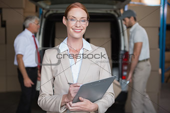 Warehouse manager writing in clipboard with delivery in background