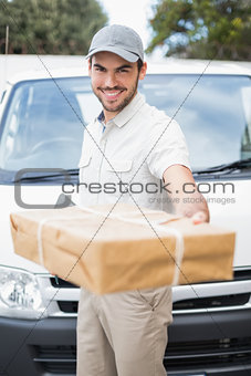 Delivery driver smiling at camera by his van offering parcel