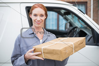 Delivery driver smiling at camera by her van holding parcel