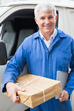 Delivery driver smiling at camera by his van holding parcel
