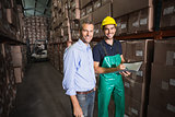 Warehouse manager smiling at camera with worker