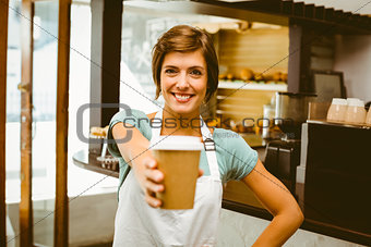 Pretty barista smiling at camera holding disposable cup