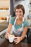 Pretty barista offering cup of coffee smiling at camera