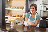 Pretty barista offering cup of coffee smiling