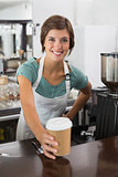Pretty barista smiling at camera holding disposable cup