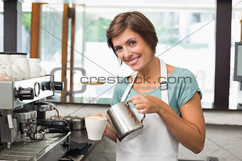 Pretty barista pouring milk into cup of coffee