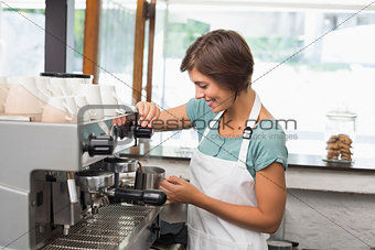 Pretty barista steaming jug of milk at coffee machine