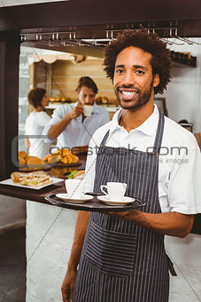 Handsome waiter smiling at camera holding tray