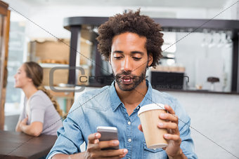 Handsome man sending a text drinking coffee