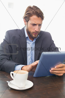 Businessman working on his tablet having coffee