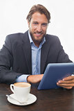 Businessman working on his tablet having coffee