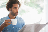 Casual man having coffee while reading newspaper