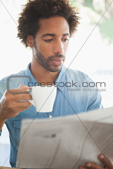 Casual man having coffee while reading newspaper
