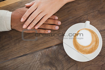 Couple holding hands beside cappuccino