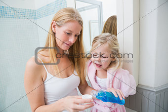Happy woman pouring blue mouthwash with daughter