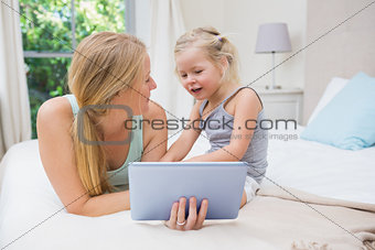 Cute little girl and mother on bed using tablet
