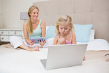 Cute little girl and mother on bed using tablet and laptop