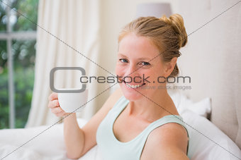 Happy blonde drinking coffee in bed