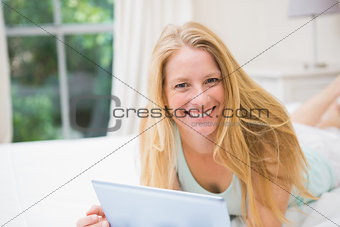 Happy blonde using tablet pc on bed