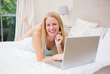 Happy blonde using laptop on bed
