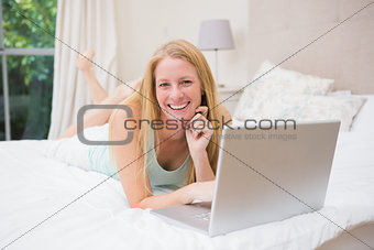 Happy blonde using laptop on bed