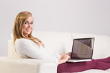 Pretty blonde relaxing on sofa with laptop