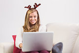 Festive blonde relaxing on sofa with laptop