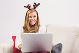 Festive blonde relaxing on sofa with laptop