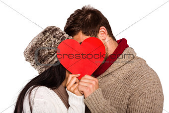 Young couple kissing behind red heart