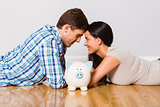 Young couple lying on floor smiling with piggy bank