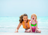 Portrait of cheerful mother and baby girl on sea shore
