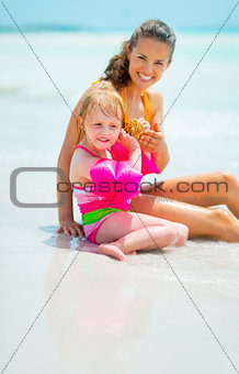 Portrait of mother and baby girl listening sound of sea in shell