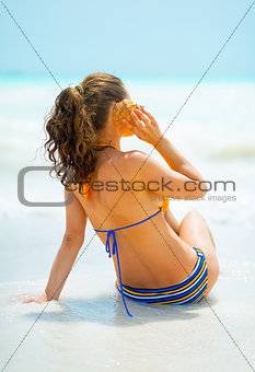 Young woman listening sound of sea in shell on sea coast. rear v